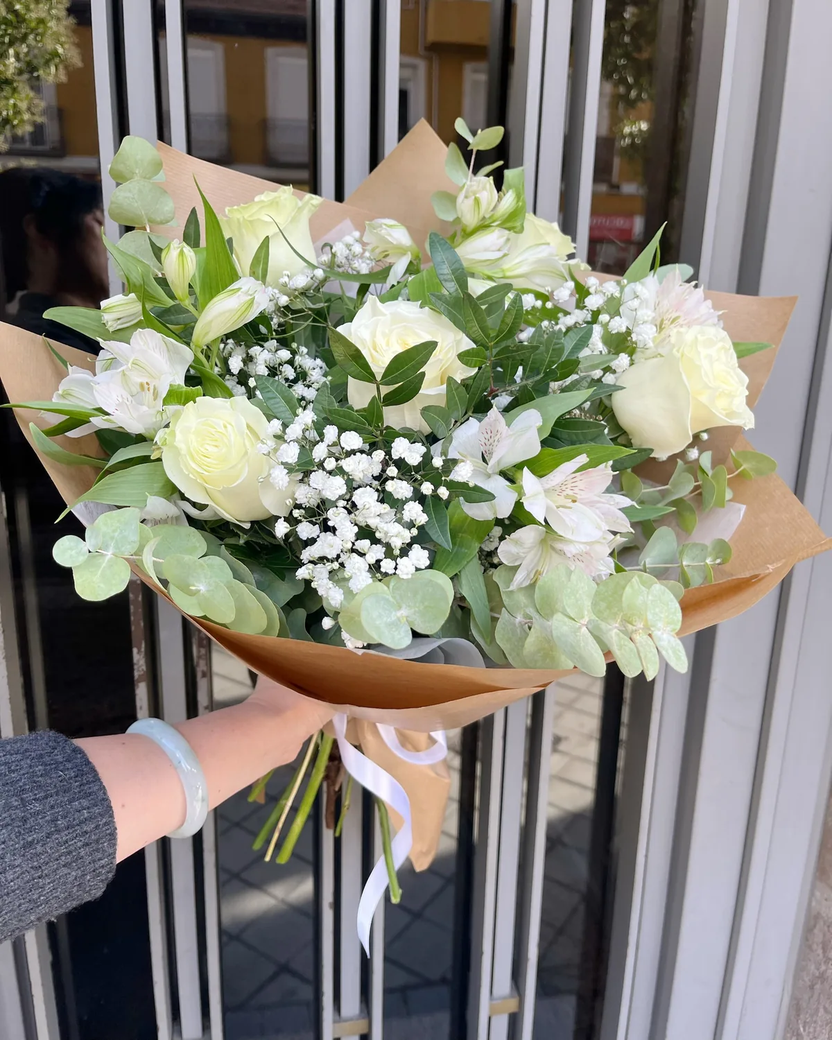 White bouquet of roses, alstroemeria and baby's breath with eucalyptus in kraft paper with a white ribbon