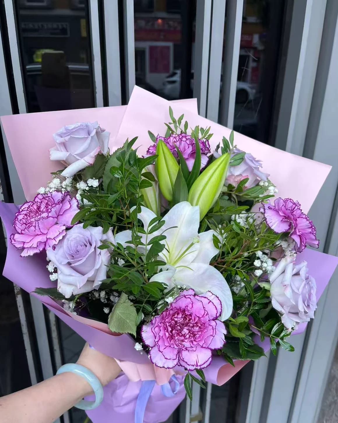 Mauve bouquet of lavender roses, violet-edged carnations and a white lily in pink and lilac Korean paper