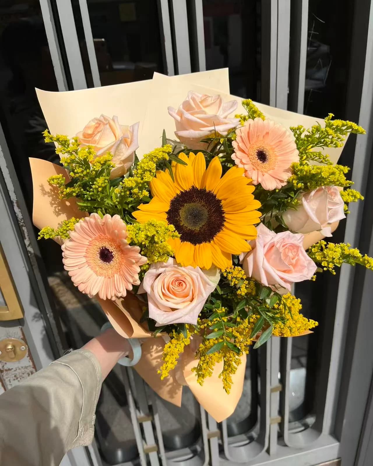 Midday bouquet with a sunflower, peach roses and gerberas and goldenrod in cream and peach paper