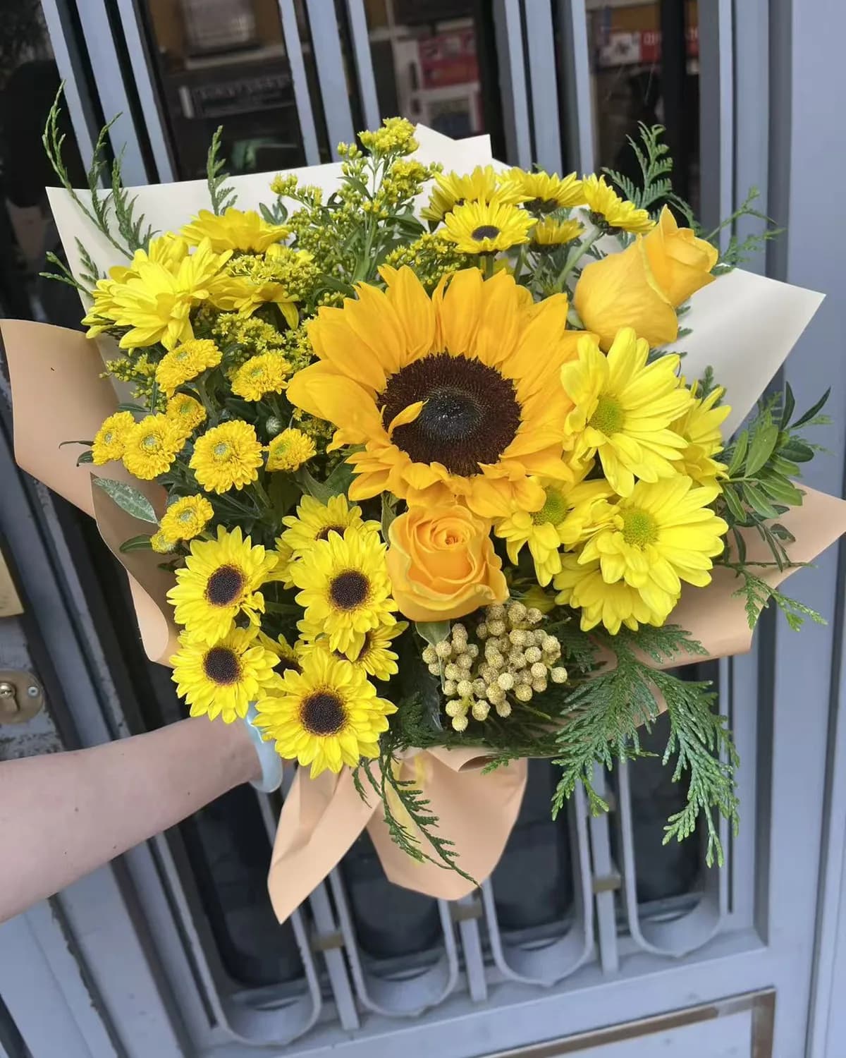 Sunbeam bouquet with a sunflower, yellow roses, daisies and mini sunflowers in cream and peach paper