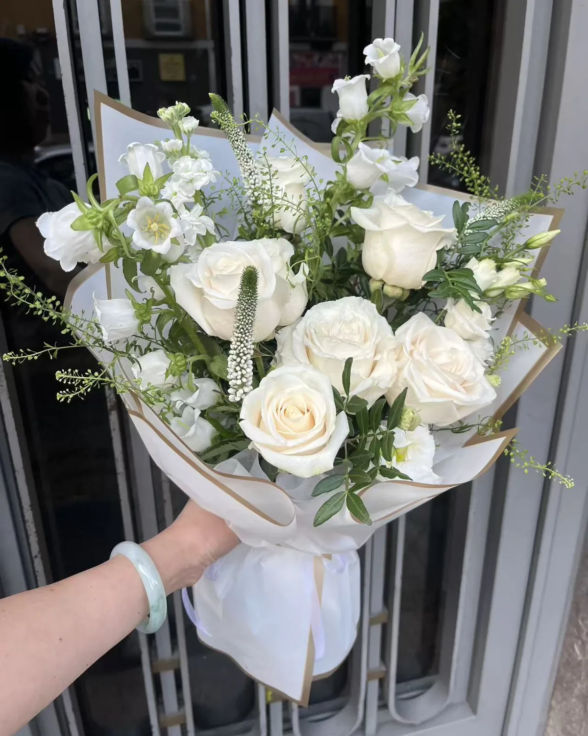 Ramo Serenidad de rosas blancas, campánulas, alhelí y verónica en papel blanco con borde dorado